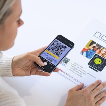 Eine Person scannt mit ihrem Smartphone einen QR-Code auf einem Informationsblatt, das Details zu einem Produkt enthält.