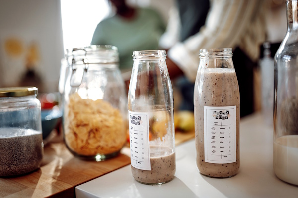 Auf der Küchentheke stehen zwei Flaschen mit Smoothies, umgeben von verschiedenen Zutaten in Gläsern und Schalen.