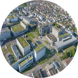 Luftaufnahme eines modernen Gewerbegebiets mit mehreren Gebäuden und begrünten Dächern, umgeben von Wohnvierteln.