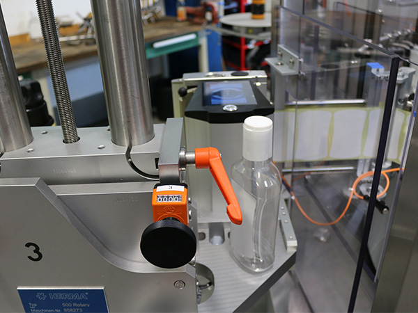 Eine Abfüllmaschine mit einem transparenten Behälter und einem orangefarbenen Hebel, bereit zum Befüllen.