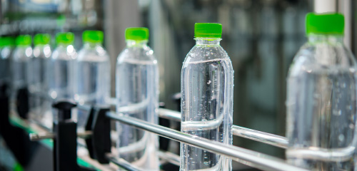 Wasserflaschen mit grünen Verschlüssen auf einem Förderband in einer Produktionsanlage.