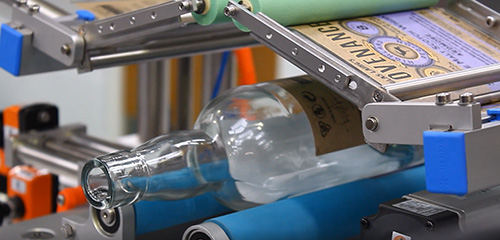 Eine Glasflasche wird auf einem Förderband bearbeitet, während sie mit Etiketten versehen wird.