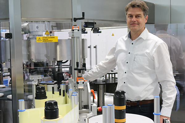 Ein Mann steht neben einer industriellen Maschine zur Verarbeitung von Flaschen, umgeben von verschiedenen Behältern und technischen Geräten.