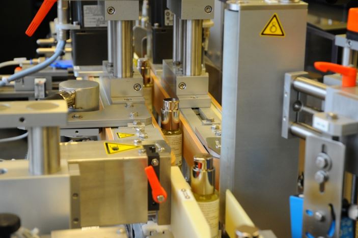 Automatisierte Maschinen zur Abfüllung von Flaschen in einer Produktionslinie, mit verschiedenen mechanischen Komponenten und Sicherheitskennzeichnungen.
