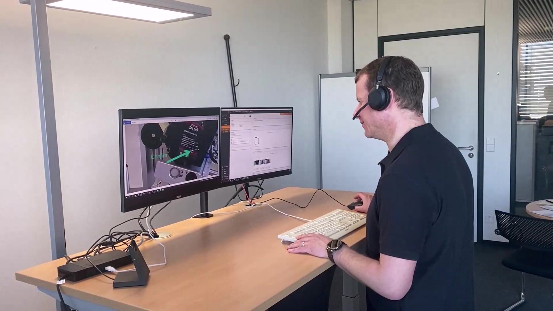 Ein Mann sitzt an einem Schreibtisch mit zwei Bildschirmen, trägt ein Headset und arbeitet am Computer.