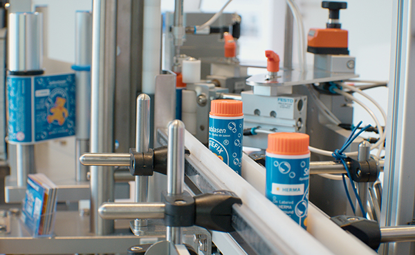 Maschinen, die Flaschen mit orangefarbenen Deckeln auf einem Förderband in einer Produktionsumgebung abfüllen.