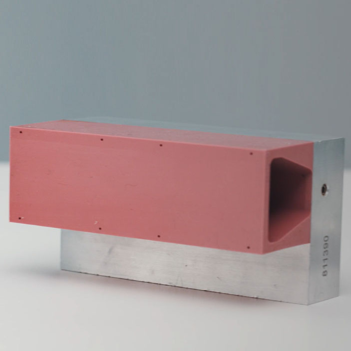 Ein rechteckiger Block mit einer roten Oberseite und einer metallischen Unterseite, mit einer Öffnung auf einer Seite.