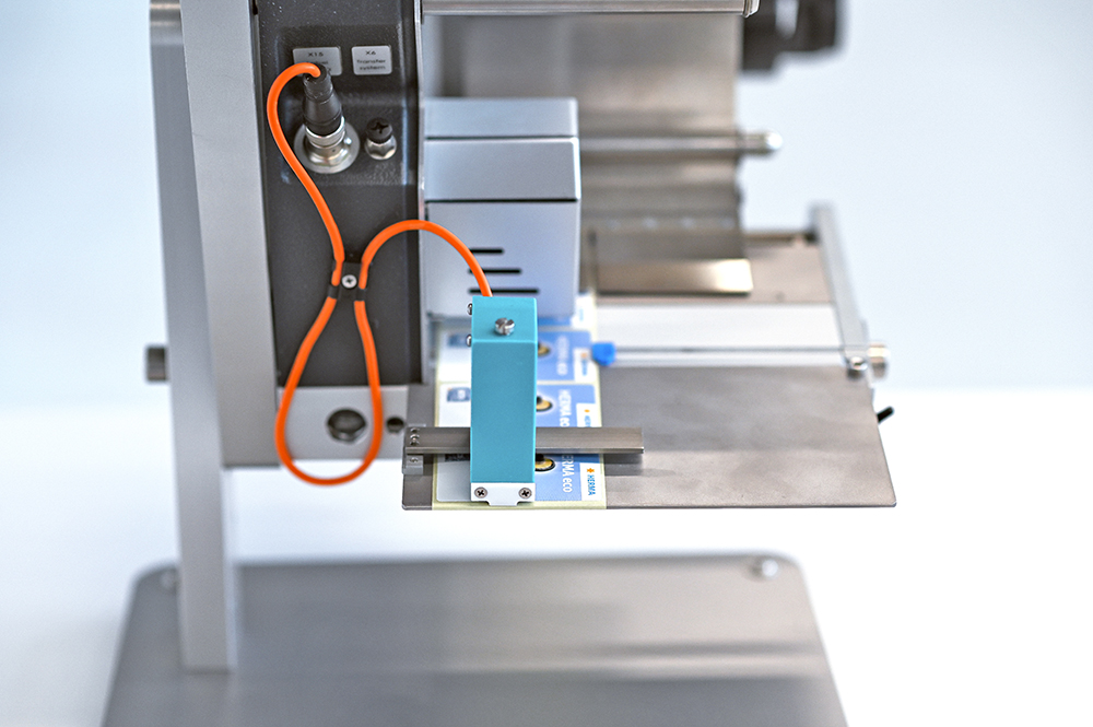 Eine technische Vorrichtung mit einem blauen Bauteil, das auf einer Metallplatte montiert ist, verbunden mit einem orangefarbenen Kabel.