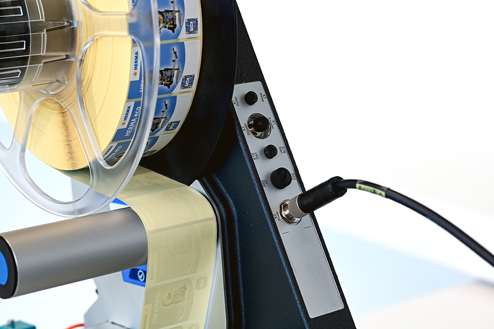 Ein Etikettendrucker mit einer Rolle gelber Etiketten und verschiedenen Anschlüssen auf der Seite.