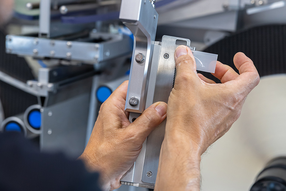 Eine Person justiert mit beiden Händen ein präzises Messinstrument, während sie an einer technischen Maschine arbeitet.