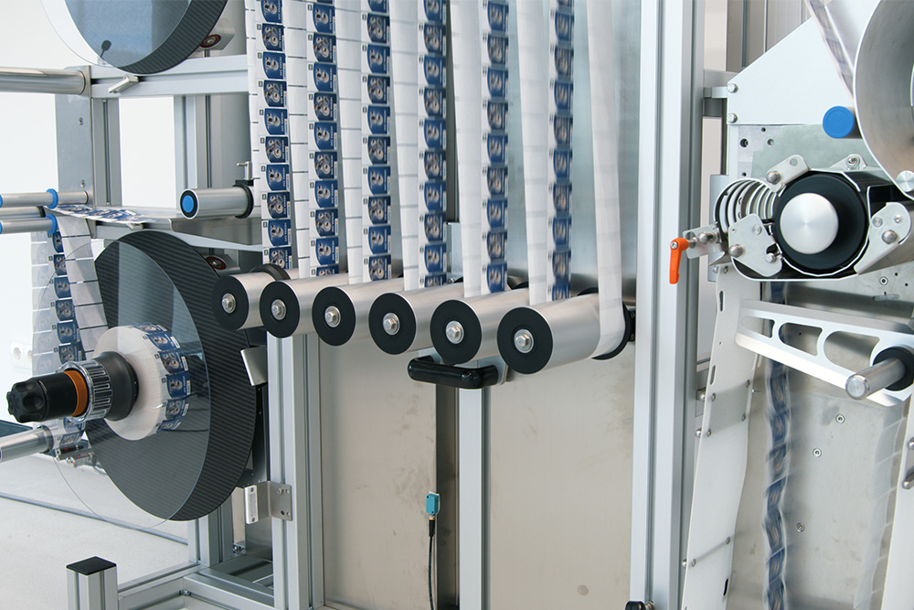 Maschine zur Verarbeitung von Bändern, ausgestattet mit mehreren Rollen und einem mechanischen System zur Anordnung der Materialien.