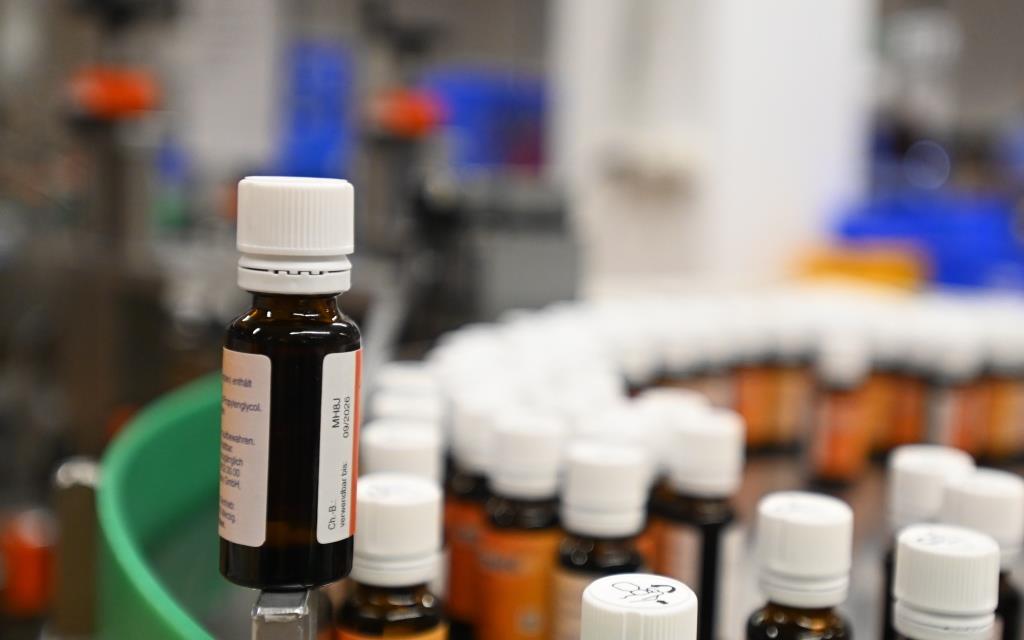 Braune Fläschchen mit weißen Kappen stehen in einer Produktionslinie, einige Fläschchen sind im Vordergrund, andere im Hintergrund.