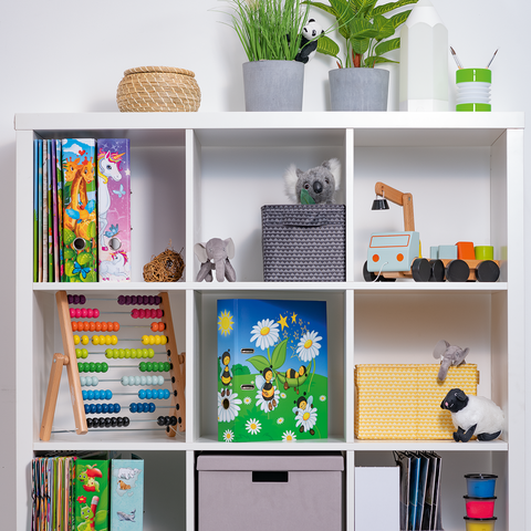 Regal mit verschiedenen Fächern, gefüllt mit Büchern, Spielzeug, Pflanzen und Aufbewahrungsboxen in neutralen Farben.