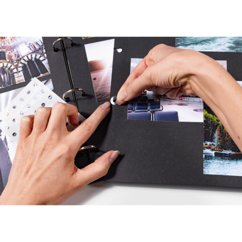 Eine Hand platziert einen Fotokleber auf einer Seite eines Scrapbooks, das mit verschiedenen Bildern und Designs gefüllt ist.