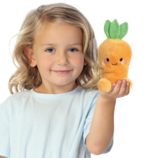 Ein kleines Kind mit blonden Locken hält ein orangefarbenes, plüschiges Karotten-Spielzeug in der Hand und lächelt.