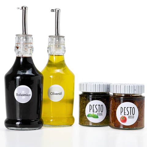 Zwei Flaschen Balsamico und Olivenöl sowie zwei Gläser Pesto in unterschiedlichen Sorten vor einem weißen Hintergrund.