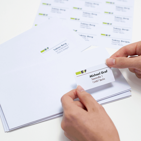 Ordner mit beschrifteten Fächern für eingehende und ausgehende Dokumente, daneben Umschläge und ein blauer Stift auf einem Tisch.