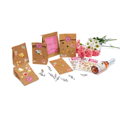 Geschenktüten mit Aufklebern, eine Flasche Sekt und Blumenarrangement. Karten mit "Danke" und dekorative Elemente sind ebenfalls sichtbar.