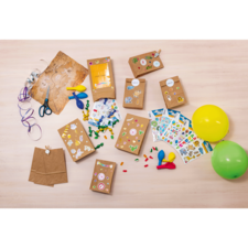 Bastelmaterialien auf einem Tisch, einschließlich brauner Papiertüten, Aufkleber, Scheren, Bänder, Luftballons und Dekorationselemente.