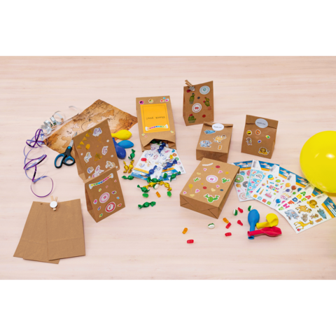 Bunte Geschenktüten und Bastelmaterialien auf einem Tisch, darunter Aufkleber, Ballons, Scheren und Süßigkeiten.