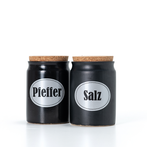 Zwei schwarze Gewürzgläser mit Korkdeckeln, beschriftet mit "Pfeffer" und "Salz".