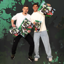 Zwei Männer posieren mit Kunstwerken, die einen Fußball und Tiere zeigen, vor einem bunten, grafischen Hintergrund.