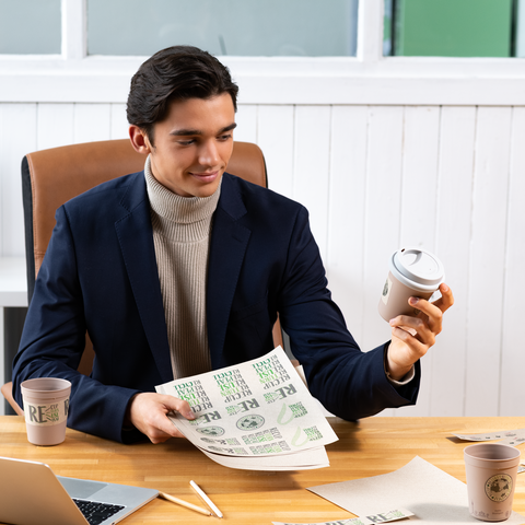Ein junger Mann in einem Anzug hält einen Kaffeebecher und ein Blatt Papier mit Text in einem Büro.