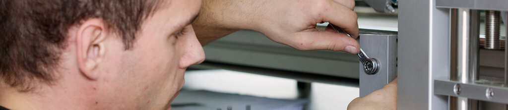 Ein Mann zieht mit einem Schraubenschlüssel eine Schraube an einem Metallrahmen an.