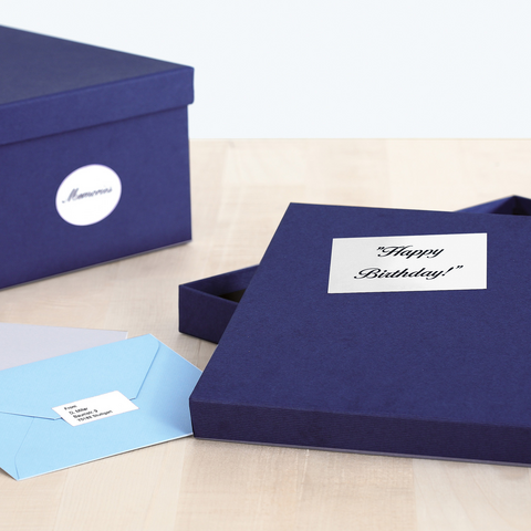 Eine geöffnete, dunkelblaue Geschenkbox mit der Aufschrift "Happy Birthday!" und zwei Umschlägen in hellblau und grau daneben.