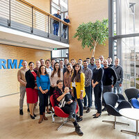 Eine Gruppe von Mitarbeitern steht in einem modernen Bürogebäude, mit einem großen Schriftzug "FIRMA" im Hintergrund.