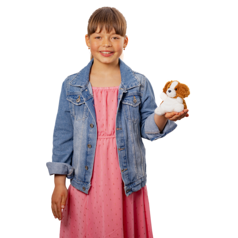 Ein Mädchen in einem rosa Kleid und einer Jeansjacke hält ein Hundestofftier in der Hand und lächelt.