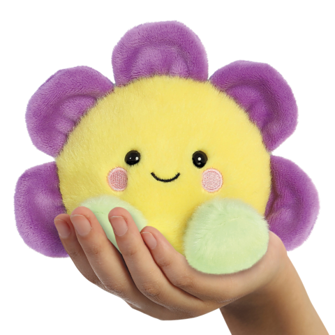 Eine Hand hält ein gelbes, lächelndes Plüschspielzeug in Form einer Blume, mit lila Blütenblättern und grünen Blättern.