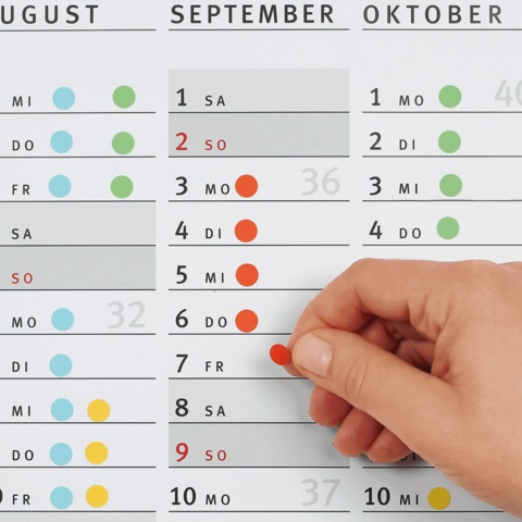 Ein Hand zeigt auf einen Kalender, der die Monate August, September und Oktober mit markierten Tagen und Zahlen anzeigt.