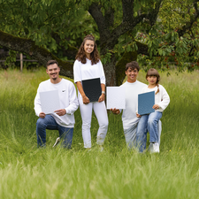 Vier Personen in weißen Oberteilen stehen und sitzen im Gras, halten jeweils Plakate mit unterschiedlichen Designs in den Händen.