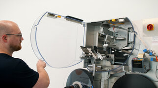 Ein Mann öffnet die durchsichtige Tür einer Maschine, die mit verschiedenen mechanischen Bauteilen ausgestattet ist.