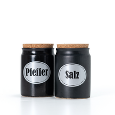 Zwei schwarze Gewürzgläser mit Korkdeckeln, beschriftet mit "Pfeffer" und "Salz".