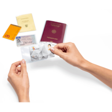 Eine Hand hält eine transparente Hülle mit einer ID-Karte, während mehrere Dokumente, darunter ein Reisepass und andere Ausweise, im Hintergrund liegen.