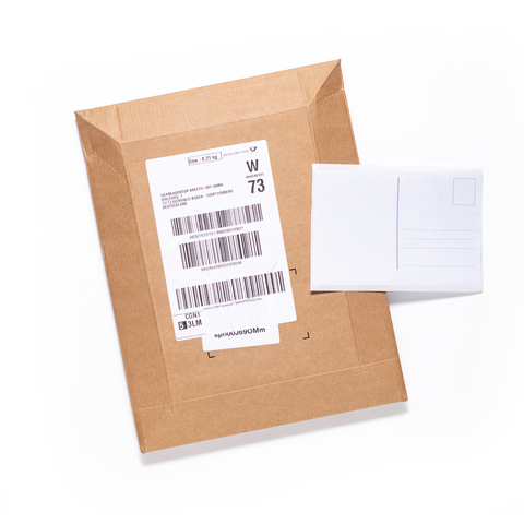 Ein brauner Versandumschlag mit einem Adressetikett und einer leeren Postkarte daneben.