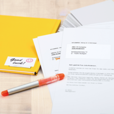 Gelbe Mappe mit Aufkleber "Viel Glück", Stift und Dokumenten, die an die ABCD-15 Company adressiert sind, liegen auf einem Tisch.