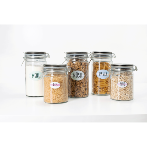 Fünf Gläser mit verschiedenen Lebensmitteln: Mehl, Reis, Müsli, Pasta und Haferflocken, jeweils mit beschrifteten Etiketten.