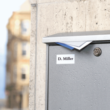 Graue Briefkasten mit dem Namen "D. Miller" auf einem urbanen Gehweg, leicht feucht von Regen.