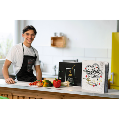 Ein junger Mann in Schürze steht an einer Küchentheke mit frischem Gemüse und einem Kochbuch mit dem Titel "Cooking with Love".