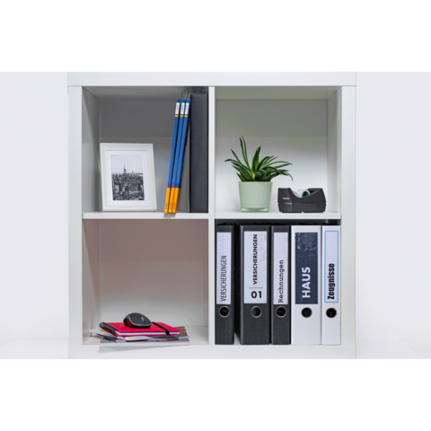 Ein Regal mit verschiedenen Fächern, gefüllt mit Aktenordnern, einem Pflanzengefäß, Bleistiften, einem Bildrahmen und einem Mauspad.