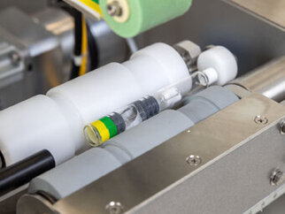 Maschinenteile mit transparenten und farbigen Behältern, die in einem industriellen Umfeld angeordnet sind.