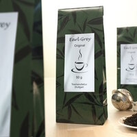 Earl Grey Tee in einer grünen Verpackung mit einem Etikett, das den Inhalt und das Gewicht von 50 g angibt." 

(Note: The text is already in German and does not require translation. It is clear and fluent as it stands.)