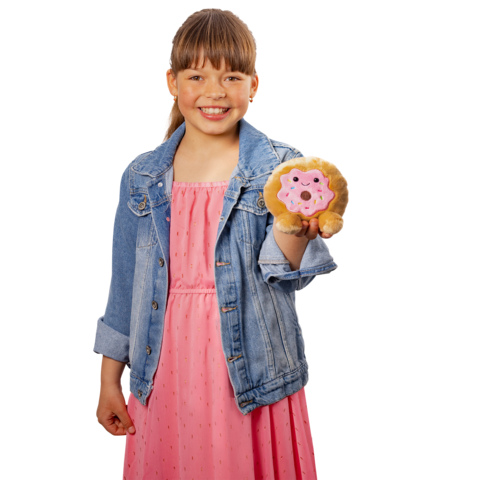 Ein Mädchen in einem rosa Kleid und einer Jeansjacke hält ein Plüschtier in Form eines Löwen und einen Donut in der Hand.