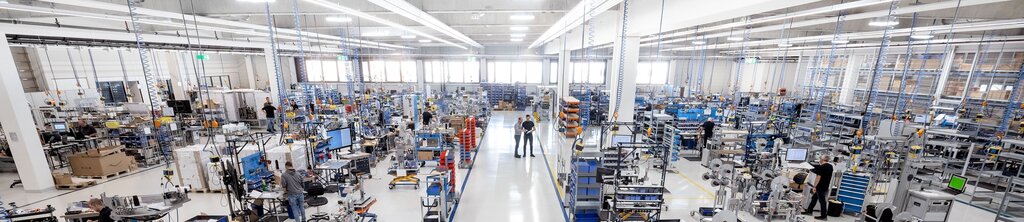 Eine große, moderne Fabrikhalle mit mehreren Arbeitsstationen, Maschinen und Mitarbeitern, die an verschiedenen Projekten arbeiten.
