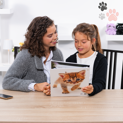 Eine Frau und ein Mädchen sitzen an einem Tisch und schauen gemeinsam in ein Bilderbuch über Katzen.