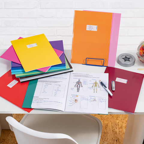 Bunte Ordner und Dokumente auf einem Schreibtisch, daneben ein Glas mit Süßigkeiten und Bürobedarf wie einen Hefter und einen Stift.