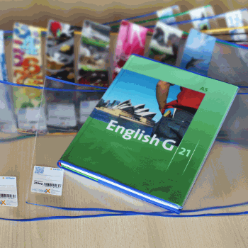 Ein Englischbuch mit dem Titel 'English G 21' liegt auf einem Tisch, umgeben von bunten, durchsichtigen Hüllen und Schreibutensilien.